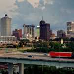 Aerial shot of Memphis, Tennessee, looking across the ramp of the Hernando de Soto Bridge towards the downtown skyline with dramatic storm clouds behind.