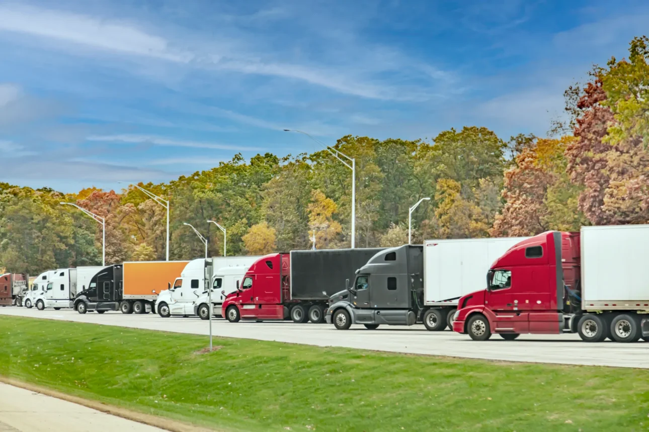 A line of semi-trucks, their cabs a variety of colors, parked