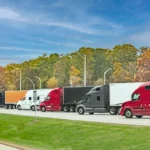 A line of semi-trucks, their cabs a variety of colors, parked