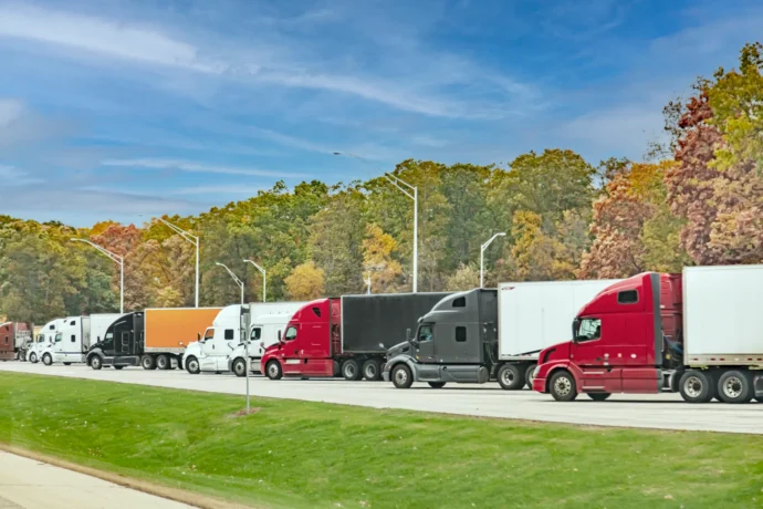 A line of semi-trucks, their cabs a variety of colors, parked